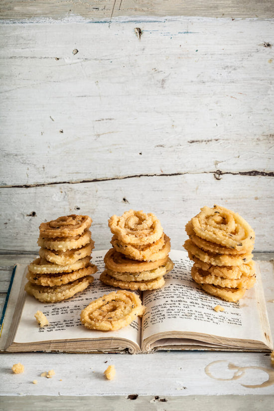 Gujarati Chakli / chakri in piles laid on top of a Gujarati Cooking book, coffee cup rings