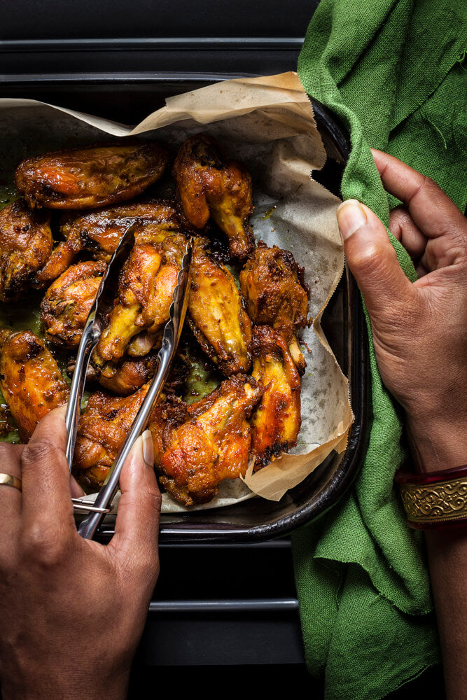 Hands serving spiced chicken nibbles with tongs from a tray