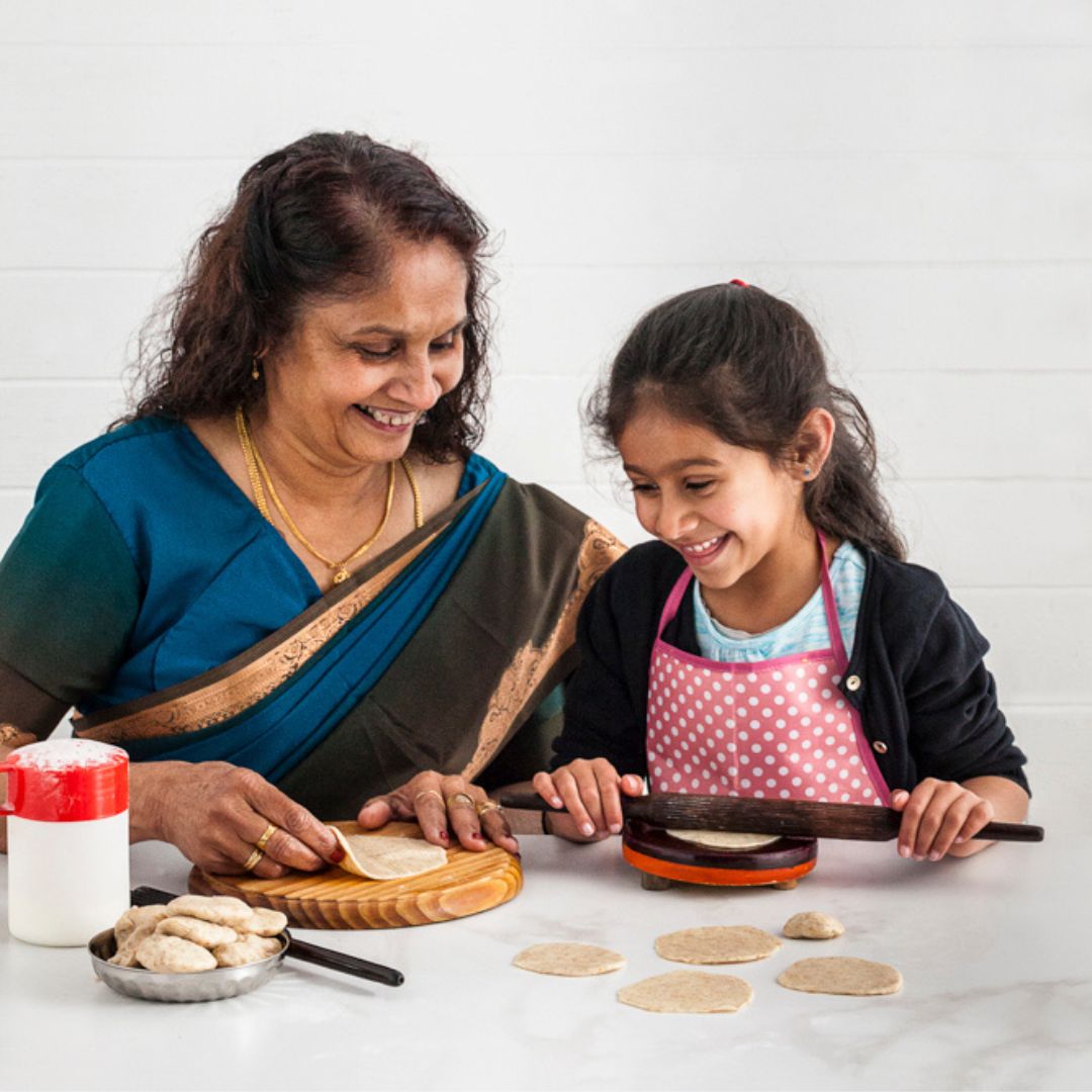Grandmother, aji, ba, mai and granddaughter making rotli, patli, rolling pin, flour